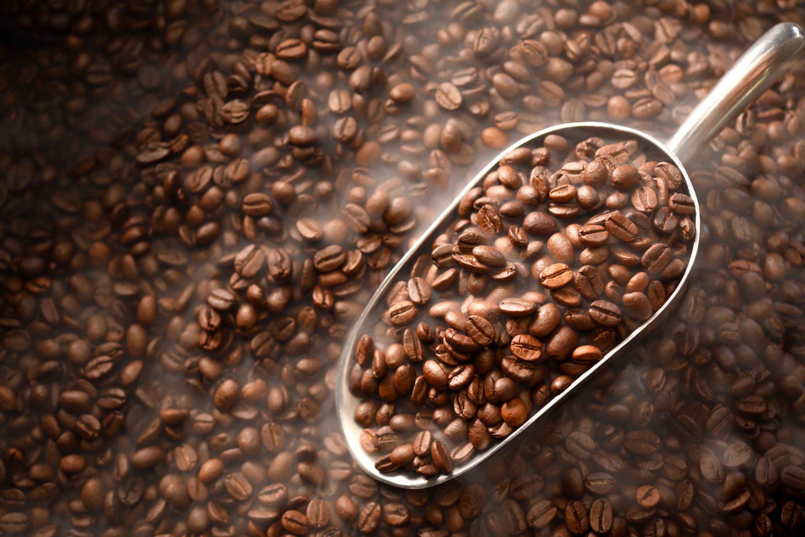 Top View Of Coffee Beans In Spoon With Smoke On Pile Of Coffee Beans