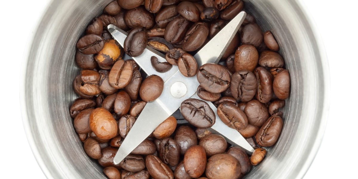 Steel coffee grinder with coffee beans isolated on white background. Close-up blade top view